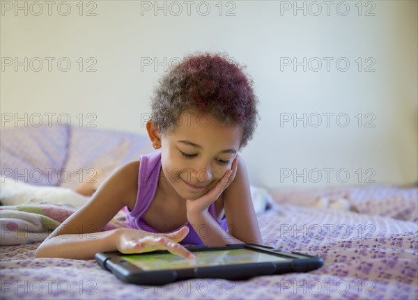 Mixed race girl using digital tablet in bed