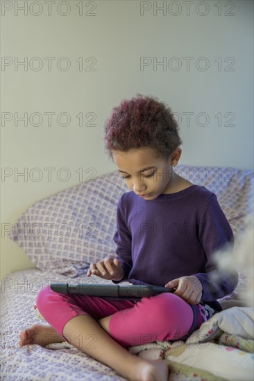 Mixed race girl using digital tablet in bed