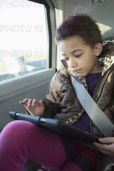 Mixed race girl using digital tablet in back seat of car