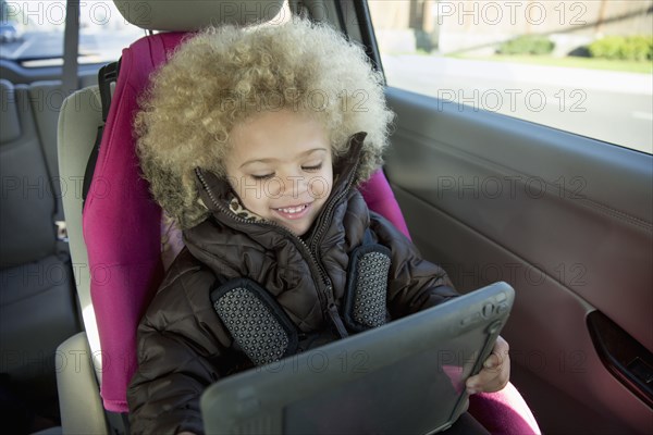 Mixed race girl using digital tablet in back seat of car