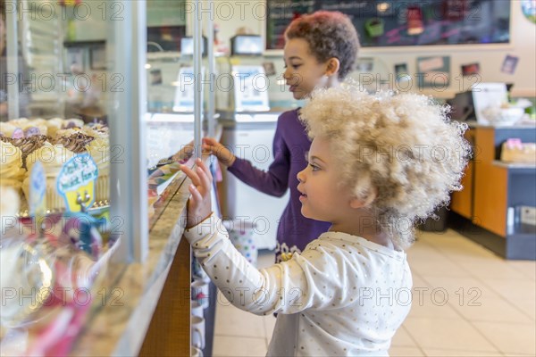 Mixed race girls picking cupcakes in bakery