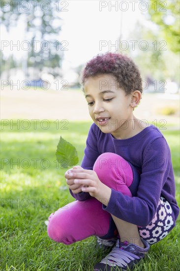 Mixed race girl examining leaf outdoors