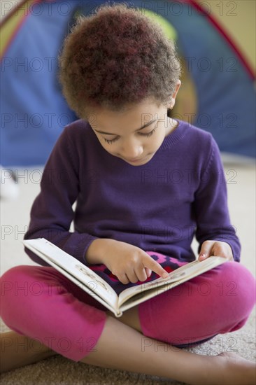 Mixed race girl reading on bedroom floor