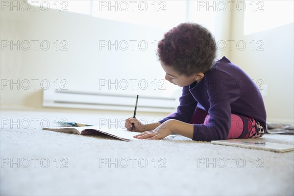 Mixed race girl drawing on bedroom floor
