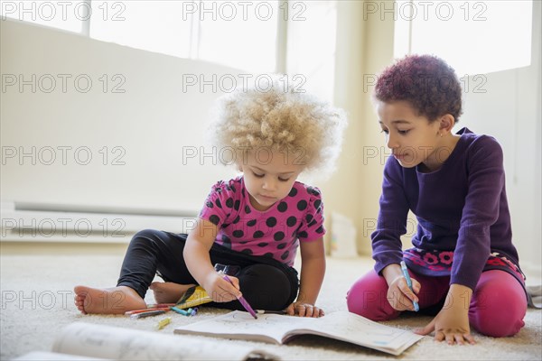 Mixed race sisters coloring on floor