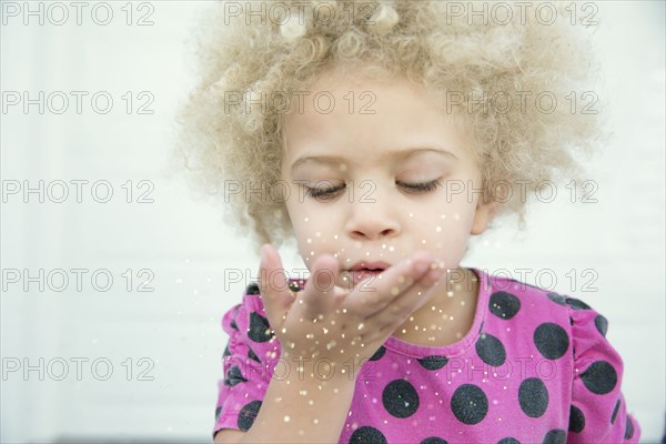 Mixed race girl blowing sparkles from hand