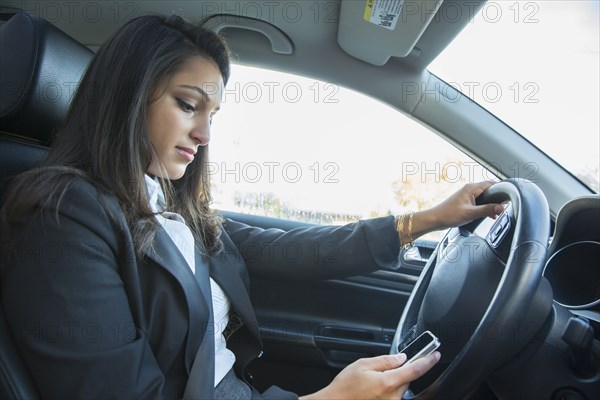 Mixed race businesswoman using cell phone while driving