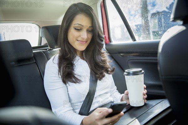 Mixed race businesswoman using cell phone in taxi