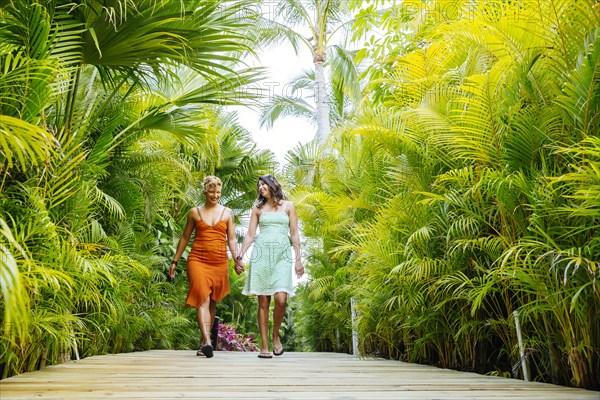 Lesbian couple holding hands on tropical walkway