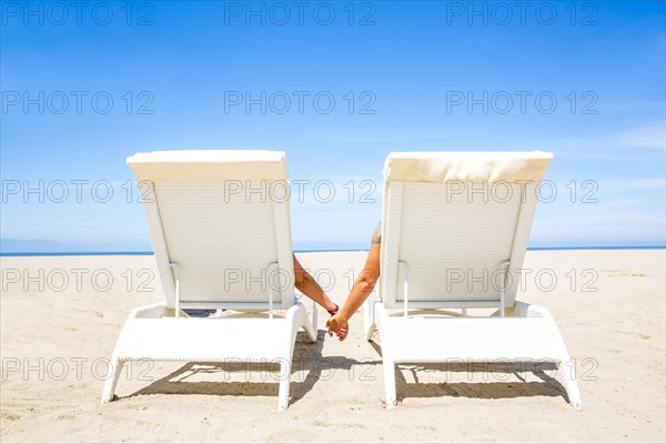 Couple holding hands in lounge chairs on beach