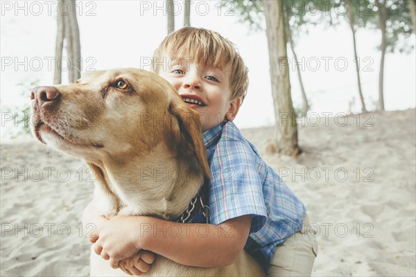 Boy hugging dog on wooded beach