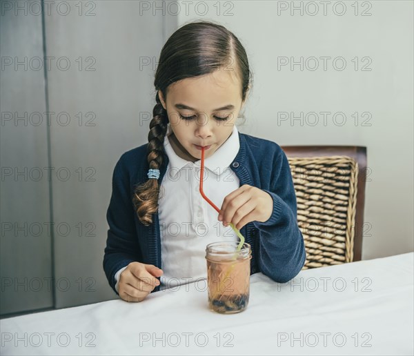 Mixed race girl drinking juice from jar through straw