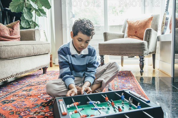 Mixed race boy playing foosball on living room floor