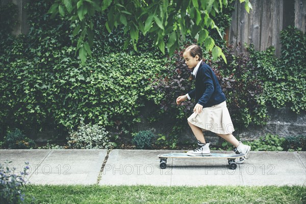 Mixed race girl riding skateboard on sidewalk