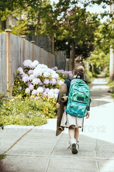 Mixed race girl carrying skateboard on sidewalk