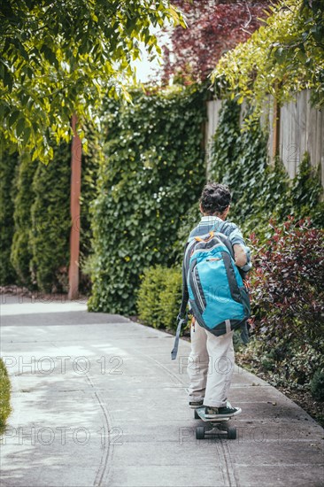 Mixed race boy riding skateboard on sidewalk