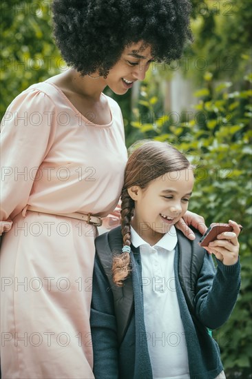 Mixed race mother and daughter using cell phone together