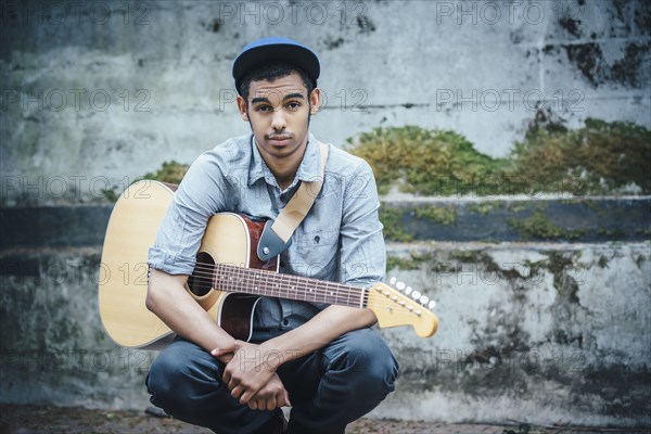 Mixed race boy with guitar crouching on urban sidewalk