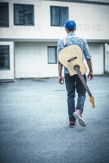 Mixed race boy carrying guitar in parking lot
