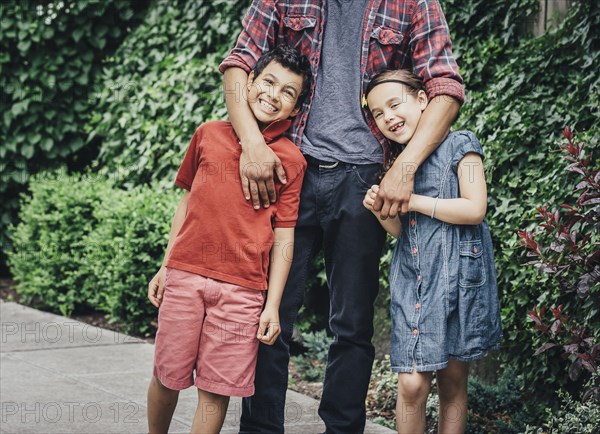 Mixed race brothers and sister hugging on suburban sidewalk