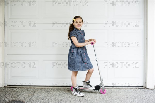 Mixed race girl smiling on scooter in driveway