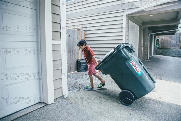 Mixed race boy pulling trash can in driveway