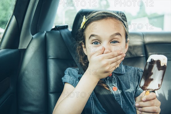 Mixed race girl eating ice cream bar in car back seat