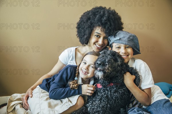 Mixed race mother and children hugging dog