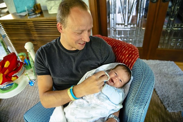 Caucasian father holding baby boy in armchair