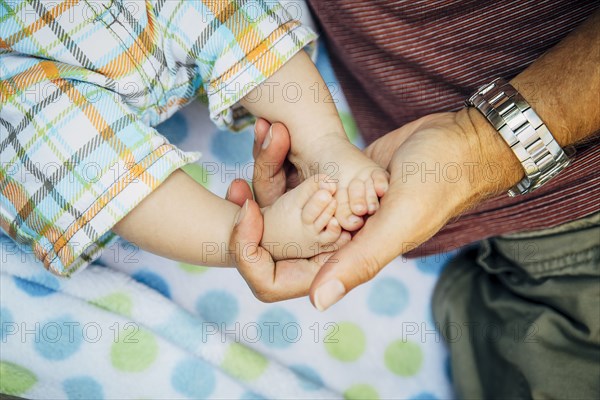 Close up of Caucasian father holding feet of baby boy