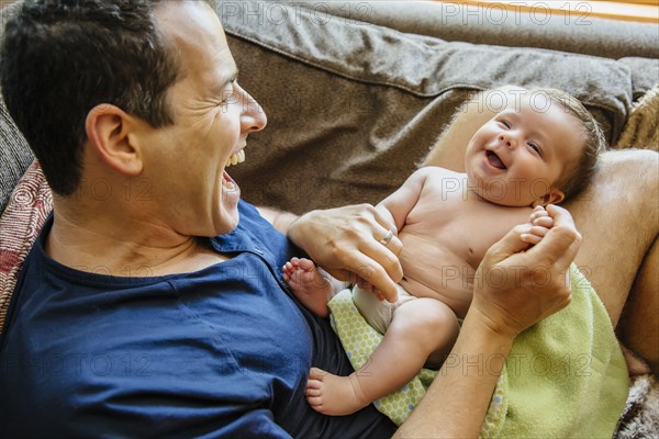 Caucasian father laughing with baby boy on sofa