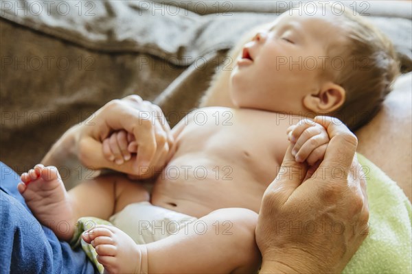 Caucasian father holding sleeping baby boy on sofa