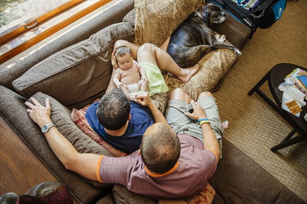 Caucasian gay couple holding sleeping baby boy on sofa