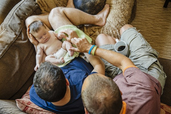 Caucasian gay couple holding sleeping baby boy on sofa