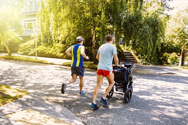 Caucasian gay couple jogging with stroller in neighborhood