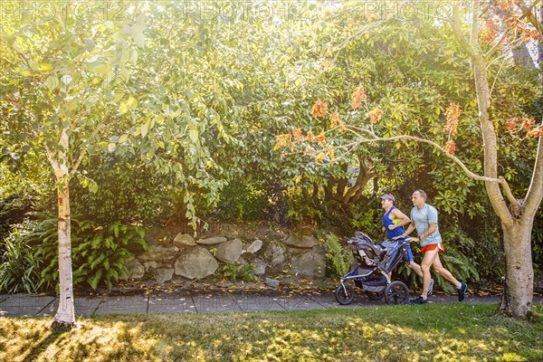 Caucasian gay couple jogging with stroller on sidewalk