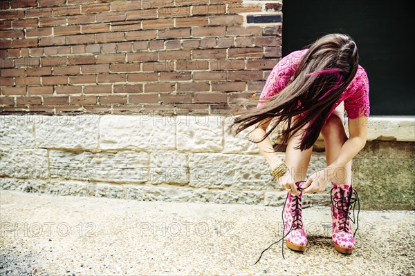 Caucasian woman tying boots on sidewalk