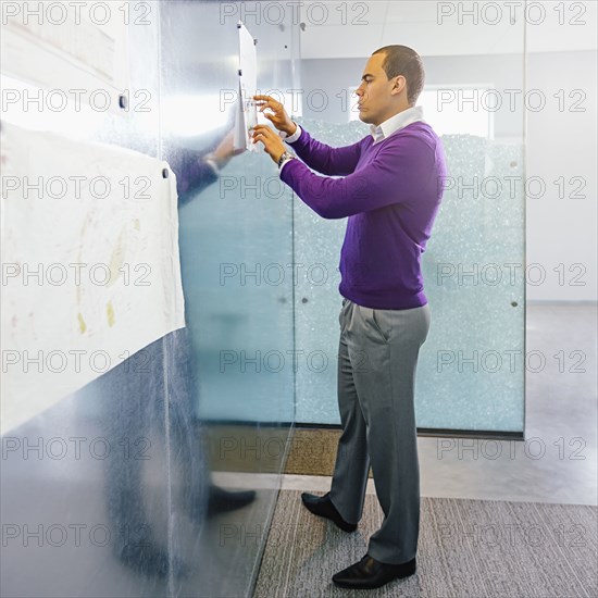 Mixed race businessman hanging paper on magnetic office wall