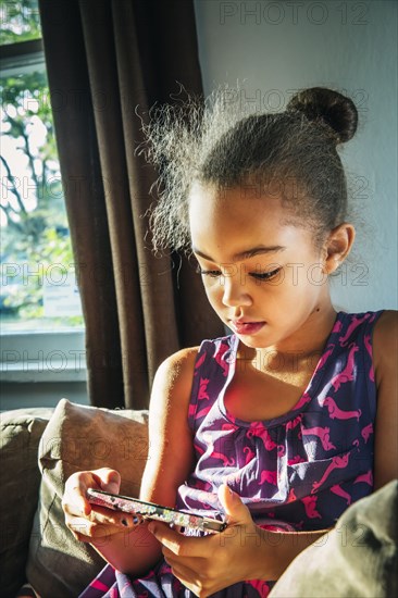 Mixed race girl using cell phone on sofa