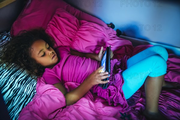 Mixed race girl using digital tablet on bed