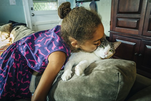 Mixed race girl kissing pet cat on sofa