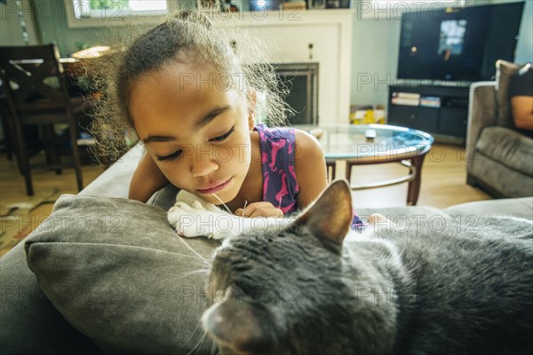 Mixed race girl playing with pet cat on sofa