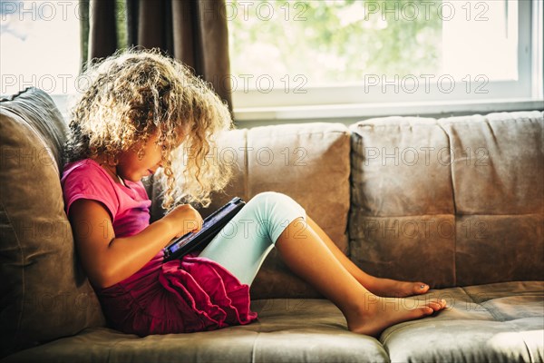 Mixed race girl using digital tablet on sofa