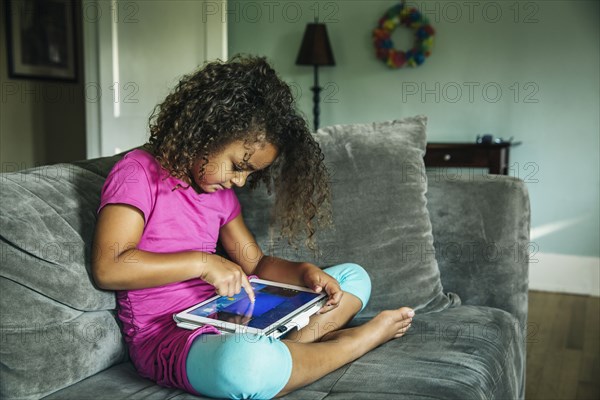 Mixed race girl using digital tablet on sofa