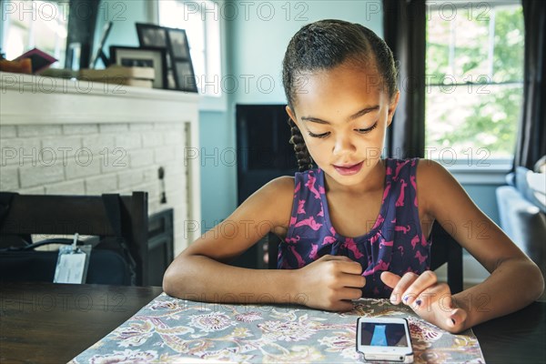 Mixed race girl using cell phone at kitchen table