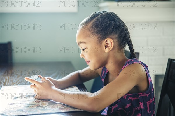 Mixed race girl using cell phone at kitchen table