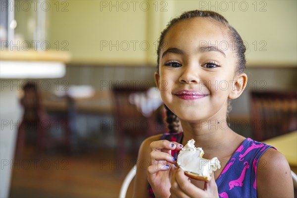 Mixed race girl eating bagel in cafe