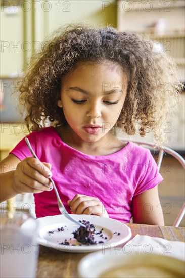 Mixed race girl eating dessert in cafe