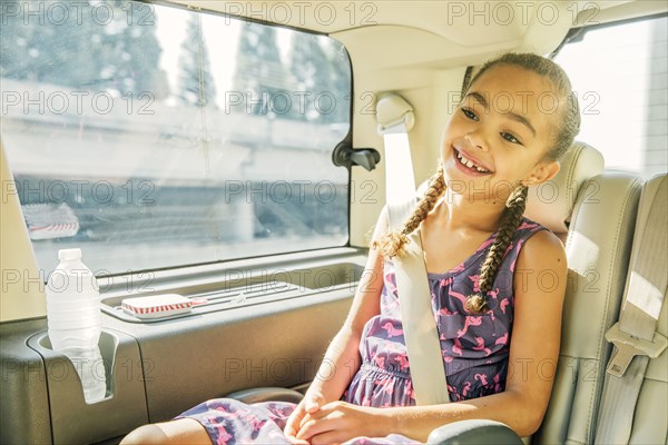 Mixed race girl smiling in back seat of car