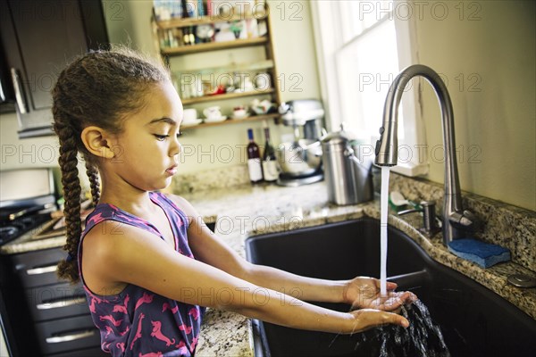 Mixed race girl washing hands in kitchen sink